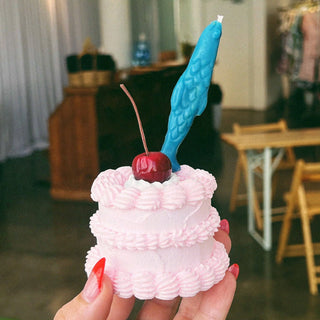 Blue sardine-shaped birthday candle standing in a mini pink cake with a cherry