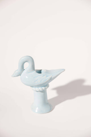 Light blue hand-glazed ceramic swan candlestick holder by St. Bingo, the swan's neck curved down so its beak rests on its breast, perched on a rope-twist collar above a flared pedestal base, shown empty