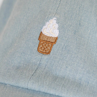 Close-up of the embroidered soft serve ice cream cone on the light denim cap, white swirl and tan waffle cone stitching