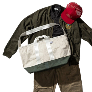 The tote styled with an olive jacket and a red cap laid out beside it, the clothing used as styling only