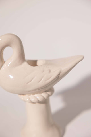 Close-up of the cream ceramic swan candlestick holder showing the glossy glaze with fine speckles, carved wing feathers, the taper socket in its back and the rope-twist collar