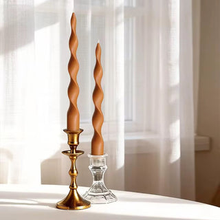 Pair of caramel twisted spiral taper candles in brass and glass holders on a sunlit table.