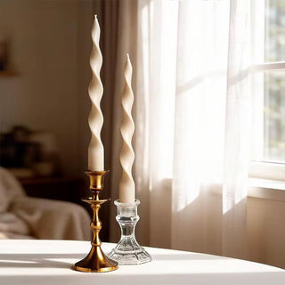 Pair of milk tea twisted spiral taper candles in brass and glass holders by a sunlit window.
