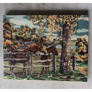 Full view of the vintage horse-and-paddock needlepoint on its stretcher bars, photographed lying on a concrete floor