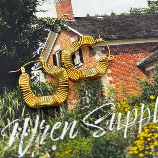 Boem Collection Lyra hoops — gold ridged squared-off hoop earrings held up in front of a brick house with flowers, Wren Supply Co. lettering across the bottom
