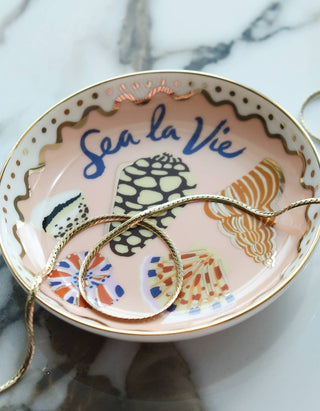 Sea La Vie seashell trinket dish on marble holding a gold chain necklace, blush ground with gold-dotted scalloped edge