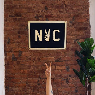 Navy NYC peace pennant hung on an exposed brick wall beside a leafy plant