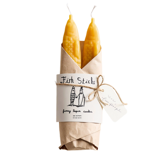 Fish Sticks beeswax taper candle pair wrapped in kraft paper like a fishmonger's parcel, with an illustrated label reading '100% beeswax, cotton wicks' and a twine bow