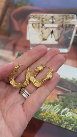 A hand holds the Boem Collection Lyra hoop earrings and turns them gently in the light to show their shape and movement — Wren Supply Co.