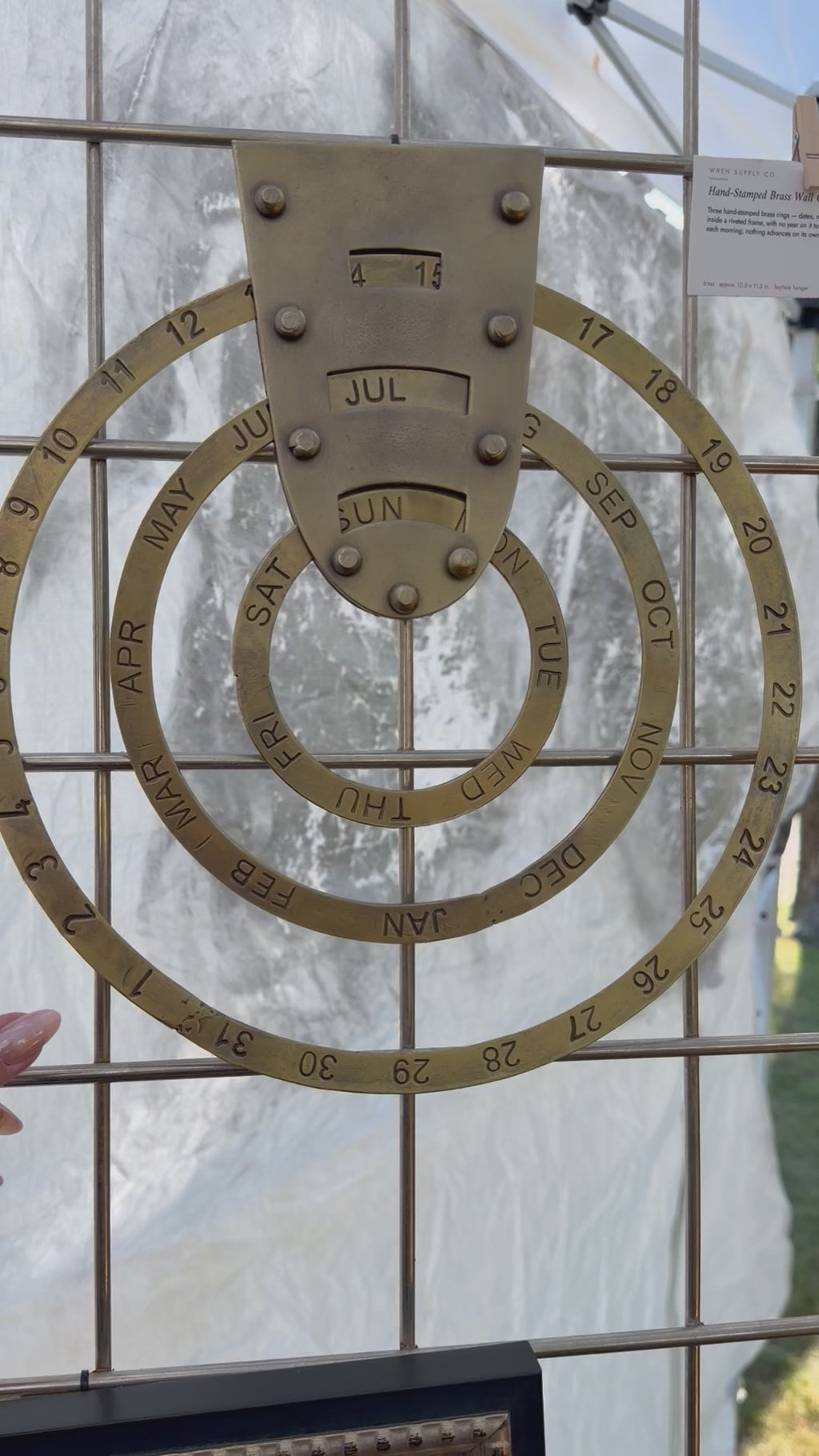 The hand-stamped brass wall calendar's three rings being spun — outer ring for the month, middle ring for the date, inner ring for the day of the week